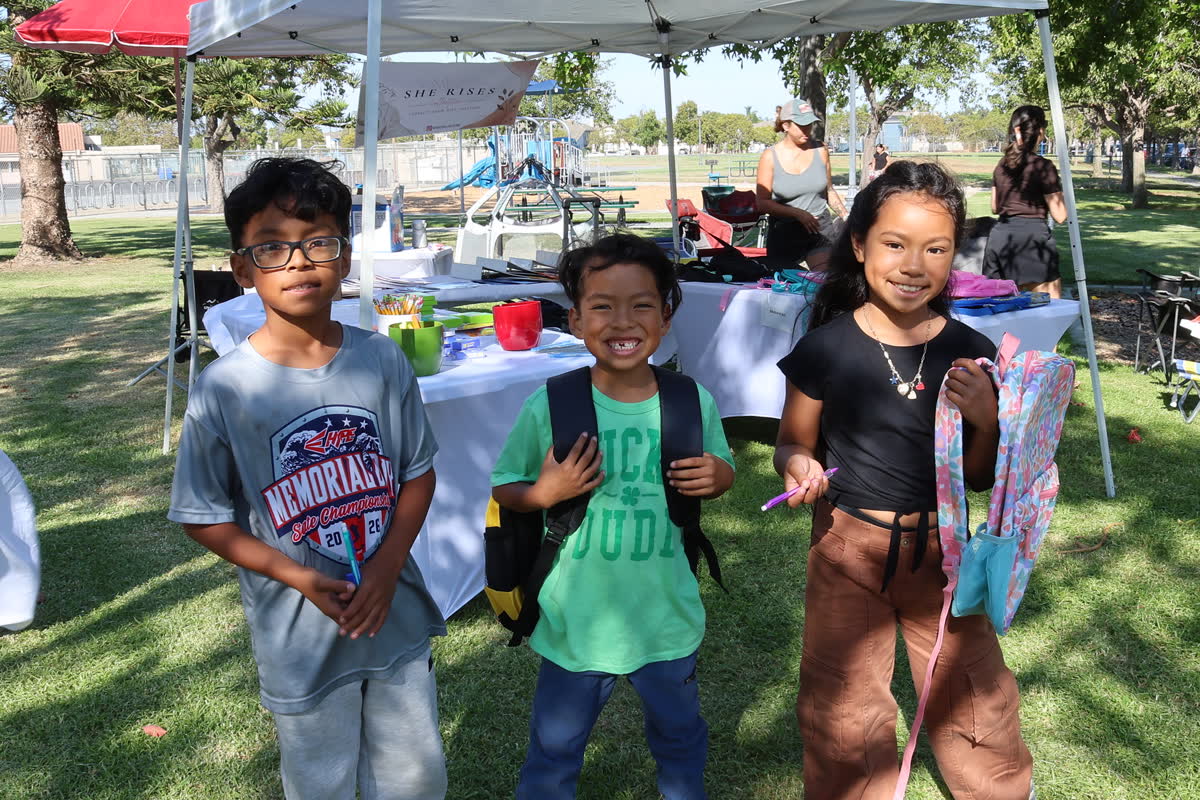 Three children standing together with new backpacks at the August 10 giveback.